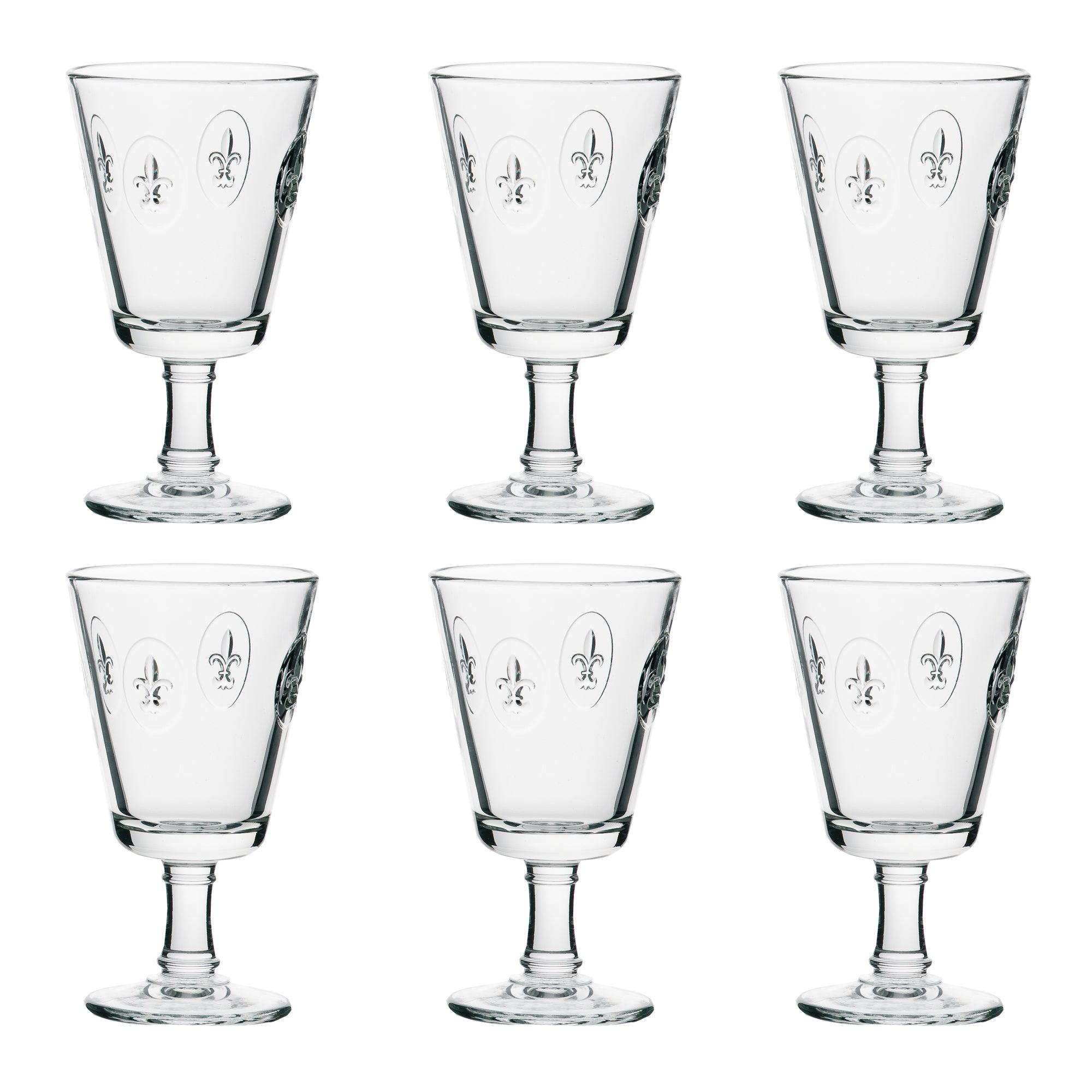 6 Fleur de Lys vinglas fra La Rochere. Glassene har en klassisk form med en bred skål og en solid stamme. Hver glas er dekoreret med et Fleur de Lys-motiv, som giver et elegant og tidløst udseende. De er arrangeret i to rækker med tre glas i hver række på en hvid baggrund