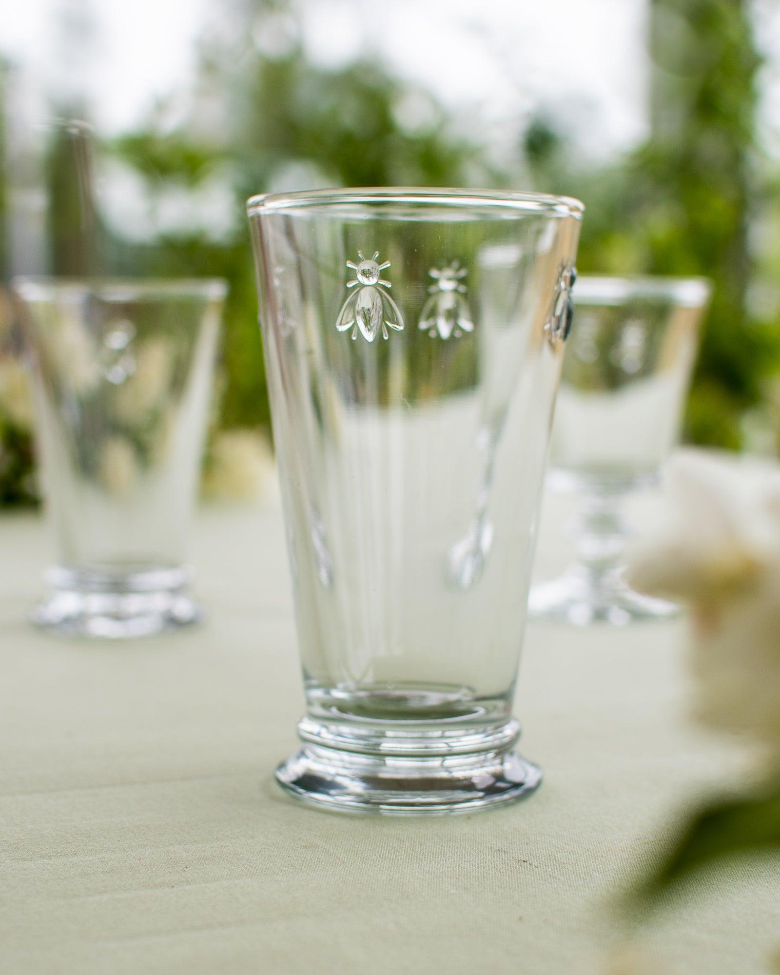 Drinksglas som står på et bord med en dug og andre glas på bordet. Man kan se naturen i baggrunden