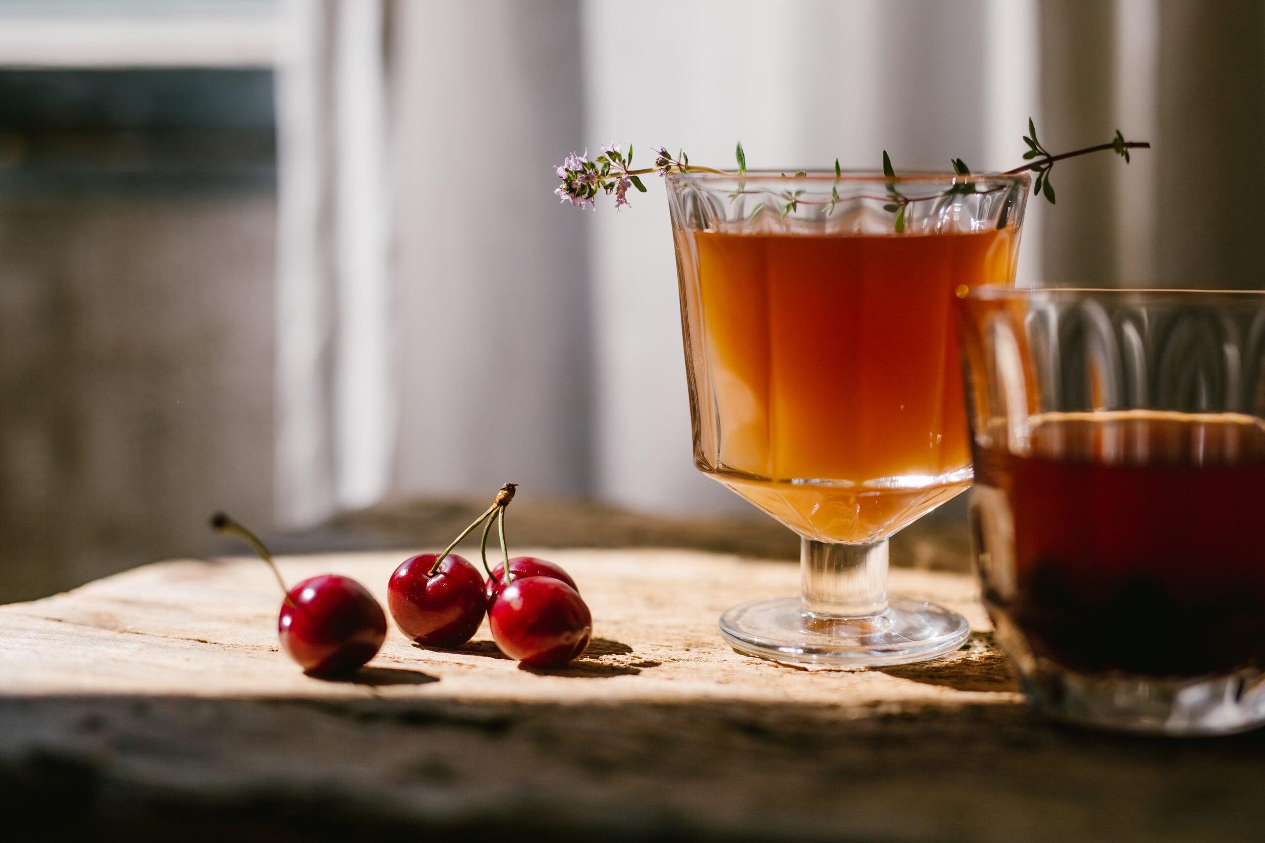 Et cocktailglas City med et orange drink i og kirsebær liggende ved siden af.