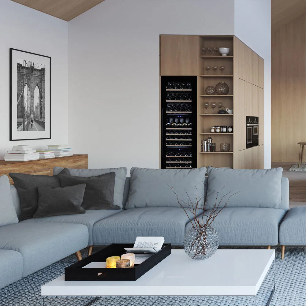 Indbygget Dunavox DX-89.246TB vinkøleskab i en moderne stue med sofistikeret interiørdesign, herunder grå sofa og minimalistiske træelementer. Ideel til elegant opbevaring af vinflasker i hjemmet.