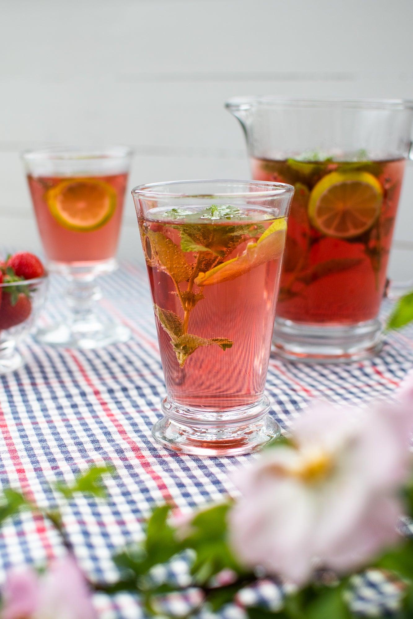 Drinksglas med en rød drink, og en kande i baggrund der er fyldt med den røde drink