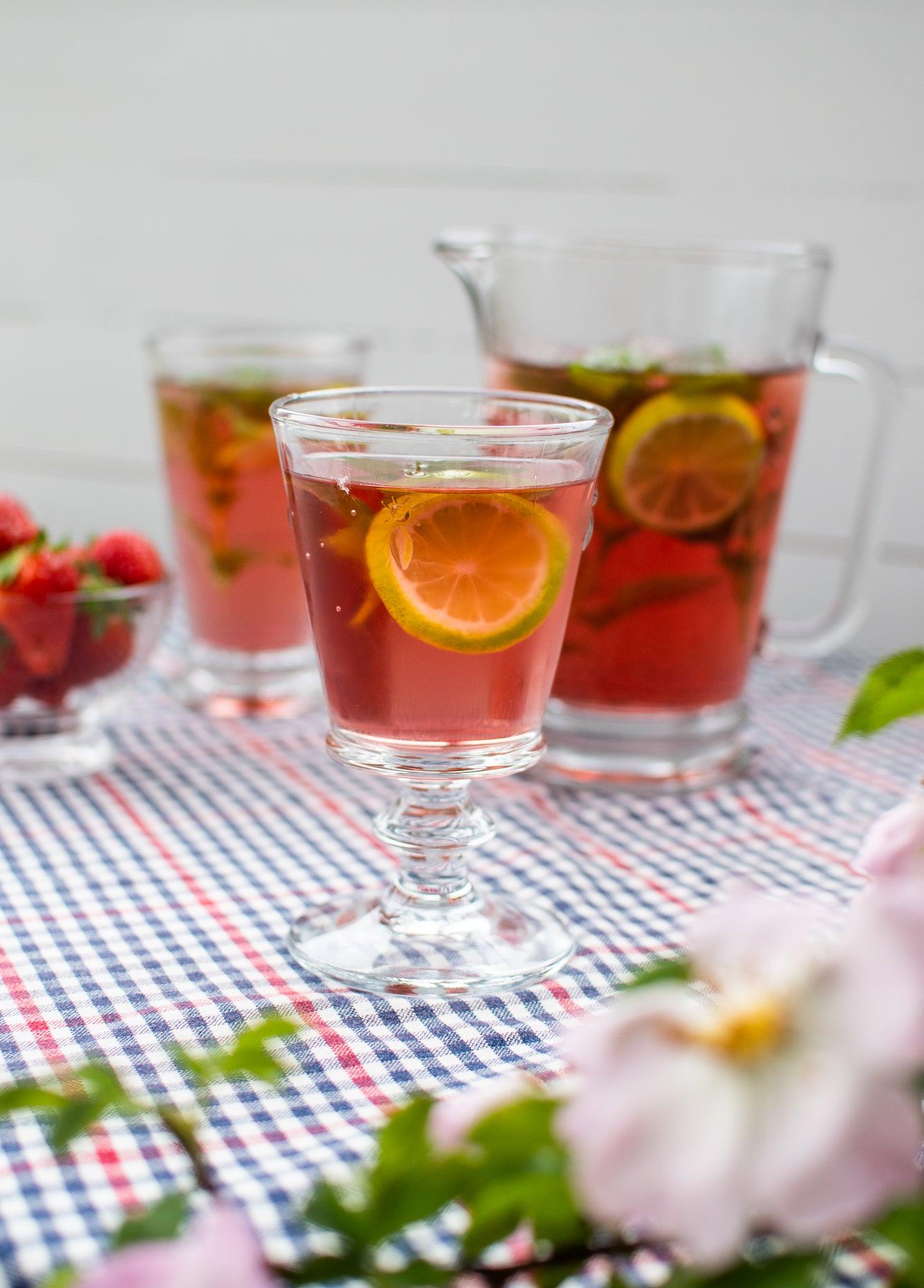 Et vinglas i Abeille stående på en ternet dug uden for med en drink og en citron i og en kande i baggrunden.