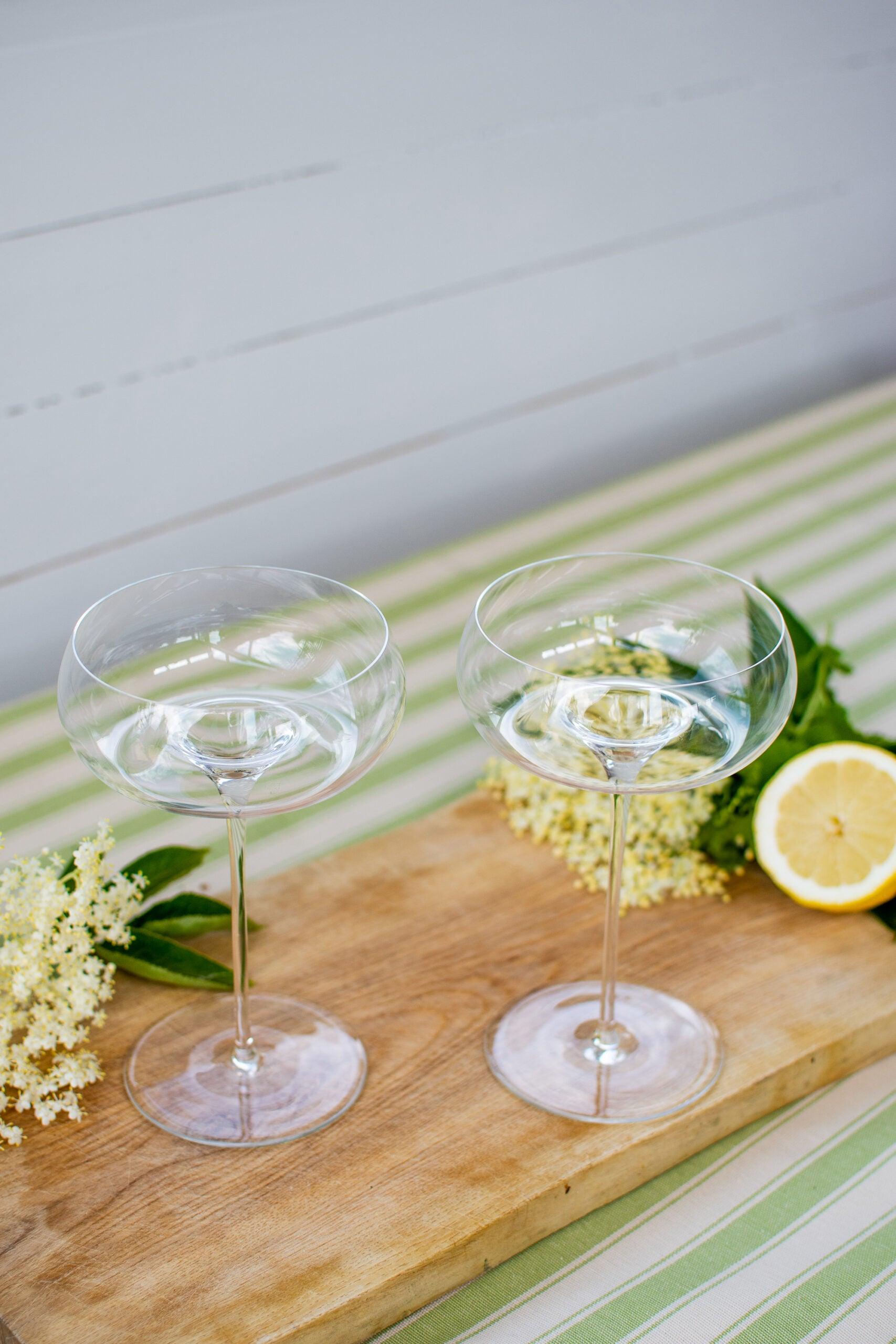 To tomme Vision Nostalgic cocktailglas stående på et bræt ved siden af en citron og hyldeblomst